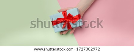 Woman holds a white gift box with a red bow on a colored background. Gift for birthday, Christmas, Valentine's Day, New year . Flat lay