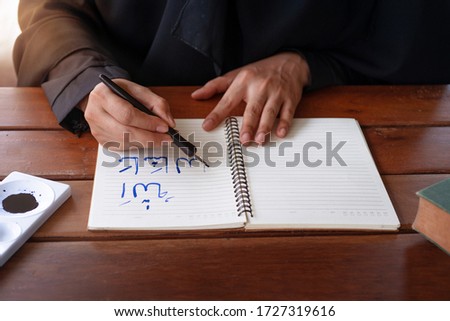 Arab Muslim woman writing Arabic handwriting with ink, Arabic letters mean the name of god "Allah" and "Prophet Muhammad"