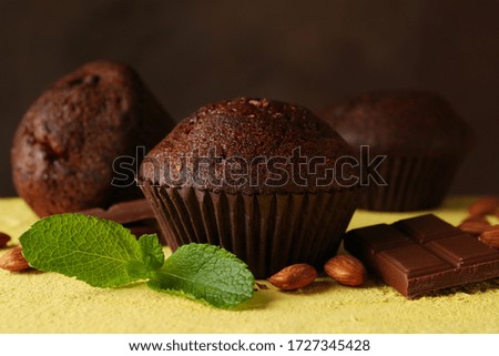 Composition with tasty muffins, chocolate and nuts on yellow table