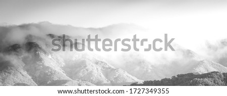 A greyscale shot of the beautiful mountain peaks barely visible through the fog Royalty-Free Stock Photo #1727349355