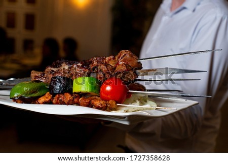 the waiter holds a plate with barbecue in restoran