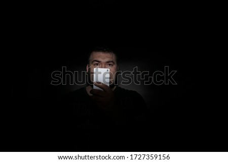 handsome middle age  man looking at far away with mobile phone surprisedly with black shirt  in front of black background. white cell phone. studio shot