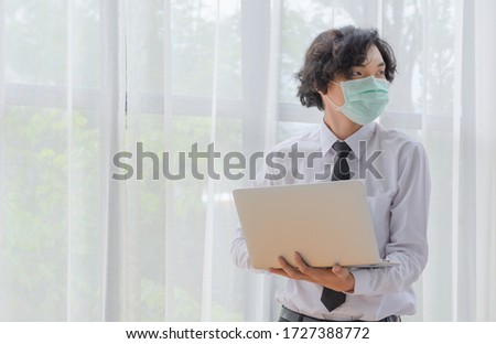 Young man wearing  a mask holding laptop 