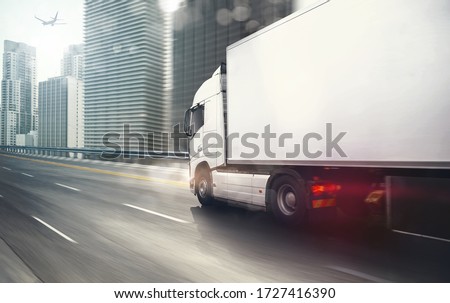 White truck moving fast on the highway with a modern city in the background