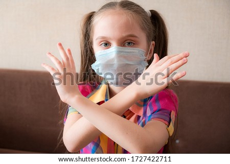 Concept of coronavirus quarantine. Child wearing medical protective mask during flu virus, making stop gesture. COVID-19. Little Girl doing stop sign with crossed hands