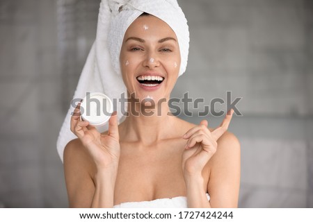 Head shot happy 30s woman with towel on head holds night or day cream jar anti-ageing beauty treatment advertises effective product, moisturizing and hydration, deep regeneration facial creme concept Royalty-Free Stock Photo #1727424244
