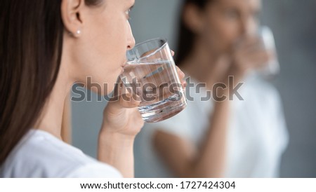 Woman reflecting in mirror standing indoors holding glass drink filtered still clear water, horizontal banner close up, dehydration prevention, care about drinking regimen aqua balance in body concept