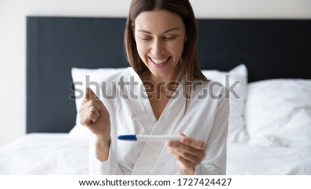 Horizontal banner image of awakened millennial woman sitting in bed holding digital pregnancy test focus on happy excited face, check ovulation period, fertility maternity, new life baby birth concept Royalty-Free Stock Photo #1727424427