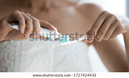 Gentle whitening toothpaste from tube being applied to soft-bristled toothbrush close up view woman hands, body wrapped in towel after shower personal self-care procedure, tooth care treatment concept Royalty-Free Stock Photo #1727424436