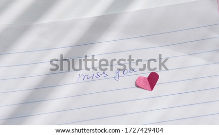 miss you note hand written on a paper. love letter with paper heart. relationship concept. distance relationship or long parting. missing love or partner. romantic reminder