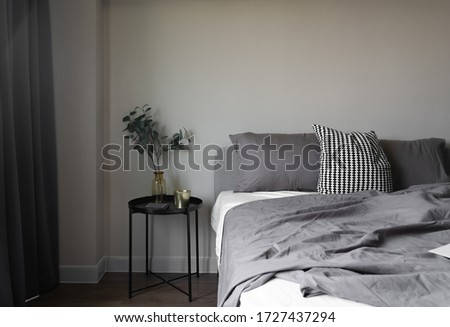 Bedroom corner soft pillows setting decorated with circular night table and with gold picture frame on beige painted wall / cozy interior design