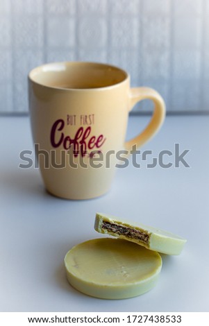 View of a coffee cup with lettering full with black coffee together with round cookies enrobed with white chocolate on white background