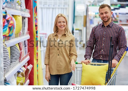 married couple shopping, buy pillows and bedding in the market. couple look at camera and smile, man hold the cart
