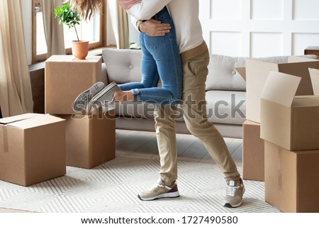 Close up legs of loving husband lifting wife, celebrating moving day, happy family having fun in living room with cardboard boxes on floor, young couple excited by relocation into first new house Royalty-Free Stock Photo #1727490580