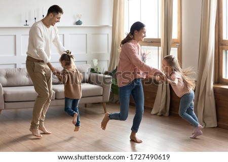 Happy parents dancing with little daughter in living room, excited mother and father holding cute preschool girls hands, moving to favorite music, spending weekend together, funny family activity Royalty-Free Stock Photo #1727490619