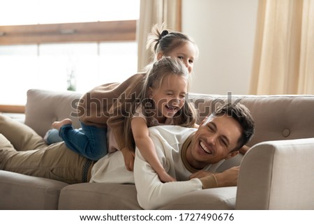 Two happy little girls playing lying on couch with father, smiling young dad having fun with preschool daughters, laughing, relaxing on cozy sofa at home, funny family activity, enjoying weekend Royalty-Free Stock Photo #1727490676