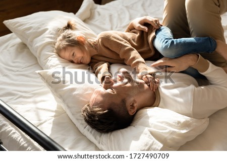 Happy father and little daughter relaxing in cozy bed together, smiling dad having fun with cute preschool girl, resting, taking nap in bedroom, family spending weekend together, enjoying free time Royalty-Free Stock Photo #1727490709