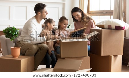 Happy parents with children unpacking cardboard boxes with belongings together, sitting on couch in new apartment, smiling mother, father and two daughters looking at family portrait in photo frame Royalty-Free Stock Photo #1727490733