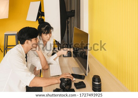 Happy Young woman Beautiful Asian model and Young male professional photographer checking pictures on computer display together after finish Enjoy working in a modern studio with equipments.