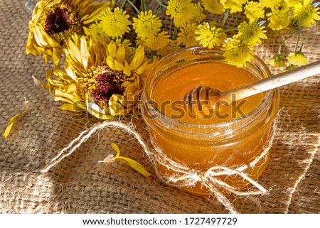 Honey jar. Dips wooden stick to glass bowl with liquid floral fresh honey. Healthy organic honey dripping, pouring from honey wooden spoon. Yellow background with flowers