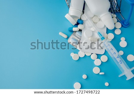 scattered variety pills, drugs, spay, bottles, thermometer, syringe and empty shopping trolley cart on blue background. pharmacy shopping concept.