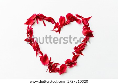 Top view of petals of red peony flowers in heart shaped form on white wooden background, copy space. Love concept, mother's day concept, feminine pattern.
