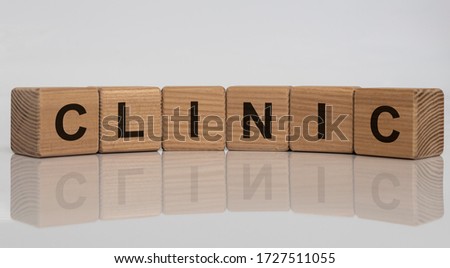 The word CLINIC written on wooden cubes isolated on a white grey glossy background with reflection