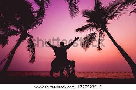 Disabled man in a wheelchair on the beach. Silhouette at sunset.