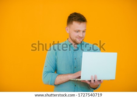 Picture of handsome man in casual t-shirt holding silver notebook and chatting or working isolated over yellow  background
