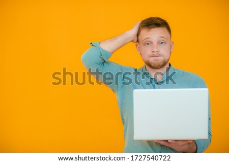 Picture of handsome man in casual t-shirt holding silver notebook and chatting or working isolated over yellow  background