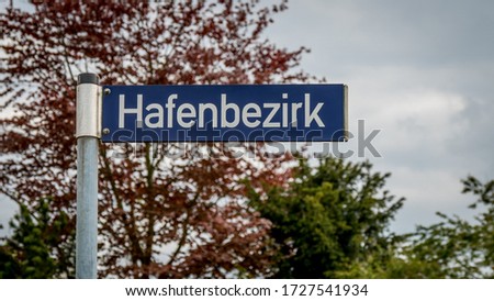 navy blue roadsign with white letters in front of a beech tree pointing to the direction of harbor district. hafenbezirk in german language