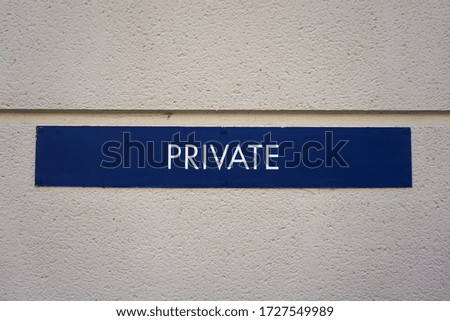 Blue private sign with white letters on a white wall.