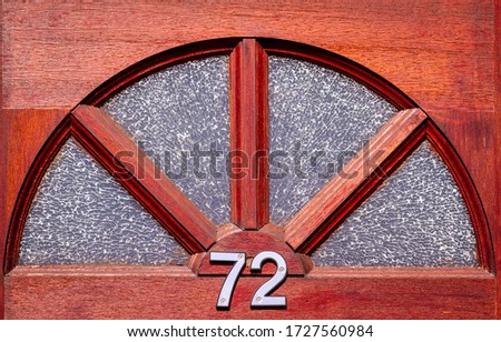 House number 72 on a wooden front door under a semicircle of broken glass
