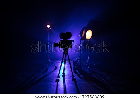 Movie concept. Miniature movie set on dark toned background with fog and empty space. Silhouette of vintage camera on tripod. Selective focus Royalty-Free Stock Photo #1727563609