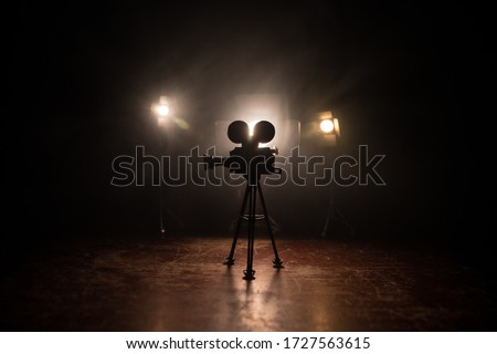 Movie concept. Miniature movie set on dark toned background with fog and empty space. Silhouette of vintage camera on tripod. Selective focus Royalty-Free Stock Photo #1727563615