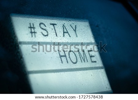 Lightbox sign with text hashtag STAY HOME behind a glass window during the rain in the evening. COVID-19. Stay home save concept.