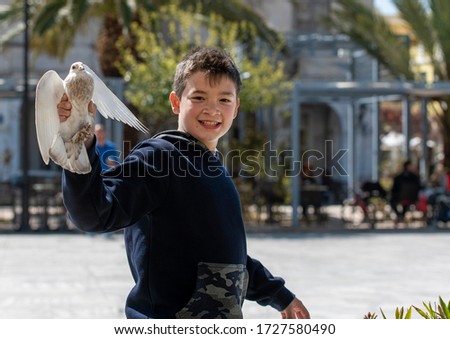 Cute and full of joy boy , is playing in the square , while feeding  the pigeons he finally managed to catch one . Enthusiasm is pictured in his face.