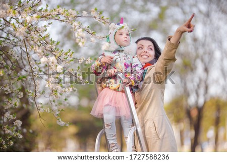 Little girls and young mother play on a stepladder in a blooming cherry garden