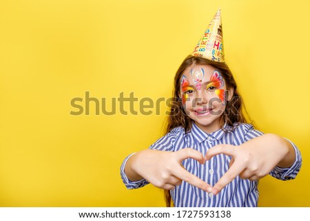 Little cute girl in birthday party hat with love sign isolated on a yellow background. Place for text, copy space.