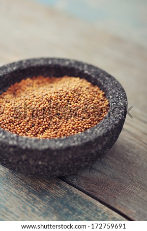 Mustard seeds in stone bowl on wooden background. Selective focus.