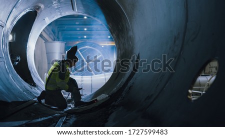 Professional Heavy Industry Welder Working Inside Pipe, Wears Helmet and Starts Welding. Construction of the Oil, Natural Gas and Fuels Transport Pipeline. Industrial Manufacturing Factory. Royalty-Free Stock Photo #1727599483