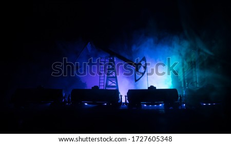 Oil pump and oil refining factory at night with fog and backlight. Energy industrial concept. Night industrial railway with oil tank wagons. Selective focus. Artwork decoration.
