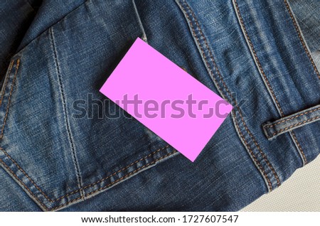Pink business card over the back pocket of jeans. Closeup of the back of a jeans with a blank form. Trade, business. View from above. Selective focus.