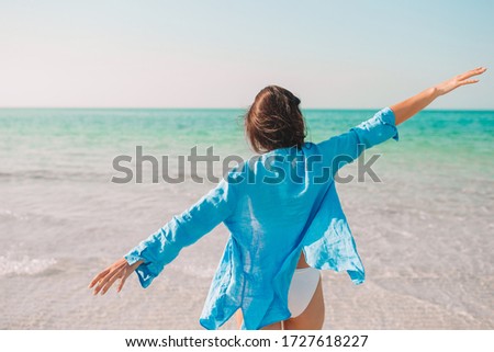 Young beautiful woman relaxing on the beach. Back view of happy girl in hat and blue shirt