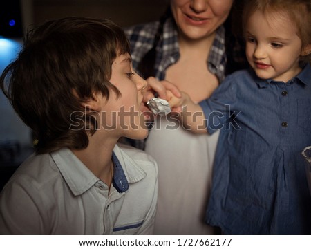 close-up. beautiful baby-girl feeds from the spoon of her brother. in the background mom is visible. a girl in a denim dress, a boy in a shirt in white and blue colors. Image with selective focus 