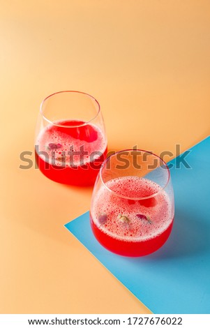 Pink alcoholic cocktail with lemonade, champagne or Martini decorated with dry rosebuds on colored background