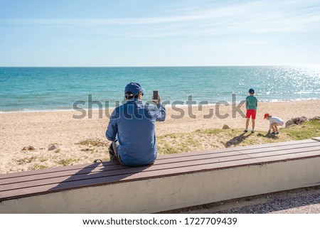 Back view of father taking sea beach pictures of kids by smart phone sunshine outdoors