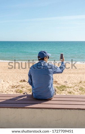 Back view of man taking sea beach pictures by smart phone sunshine outdoors
