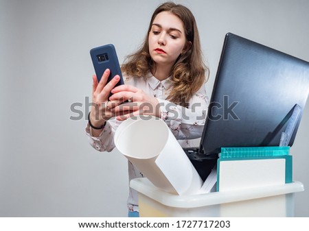 Girl wants to call. Concept - girl was fired from work. Dismissed woman with the phone. Job search online. Concept - girl is being interviewed by video link. Box with personal items. Unemployment.