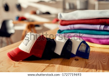 Custom apparel, clothes neatly folded on shelves. Stack of colorful clothing and baseball caps in the store. Horizontal shot. Selective focus Royalty-Free Stock Photo #1727719693